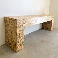 a wooden bench sitting on top of a cement floor next to a white wall in an empty room