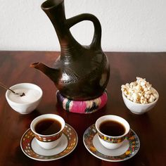 there are two cups and saucers on the table next to a teapot with popcorn in it