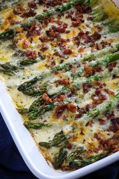 a casserole dish with asparagus, bacon and cheese in it on a blue cloth