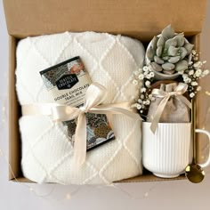 an open box containing two white towels and a coffee mug, with a succulent plant in it