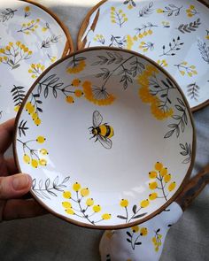 a person holding three plates with yellow flowers and a bee on them in front of the plate