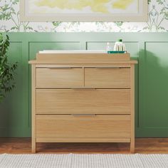 a wooden dresser sitting in front of a green wall with a painting on the wall