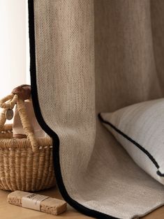 a wicker basket sitting next to a window with a curtain in the back ground