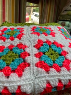 there is a crocheted blanket on the bed with red, green and blue flowers