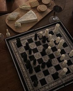 a chess board with several pieces of cheese on it and wine glasses next to it