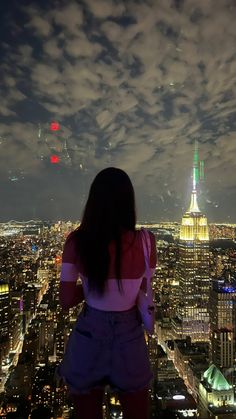 a woman standing on top of a tall building looking down at the city lights and skyscrapers