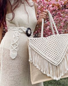 a woman in a white dress is holding a straw bag with fringes on it