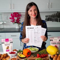 a woman standing in front of a counter holding up a paper with food on it