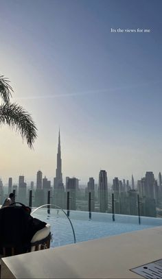 a table with a laptop on top of it next to a swimming pool in front of a cityscape