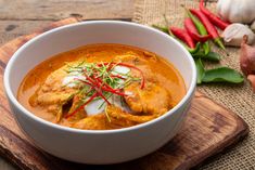 a white bowl filled with food on top of a wooden cutting board next to garlic and red peppers