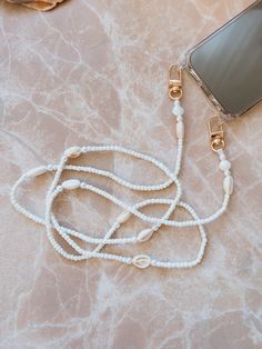 "⋒ Our SiennaFox White Beaded Phone Chain will be a perfect gift for your bestie.  Take your cell phone on every adventure in style and hands free!  This Beaded Phone Chain is a perfect addition to your beloved phone. ⋒ Designed and made for comfortable wearing on shoulder as a cross body. ⋒ This is a perfect gift for you and your bestie. Unique and beautifully made, with a boho, beachy aesthetic. It can also be used as a small bag or small purse strap!  The clasps easily attach the strap to anything you like. Makes a perfect gift for your loving family member or friend!  ⋒ HIGH-QUALITY MATERIAL:  * Made out of 3mm beads, Nylon cord and \"gold\" embellishments.  * Sizes vary, please choose the one that best fits you.  * Each piece chain will come with a universal transparent tab that you c Phone Charms Necklaces, Boho Beachy Aesthetic, Phone Hand Strap, Diy Phone Chain, Phone Strap Beads, Phone Necklace, Beaded Mobile, Summer Phone, Beachy Aesthetic