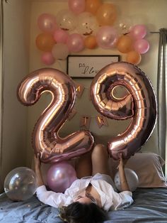 a woman laying on top of a bed next to balloons in the shape of the number twenty