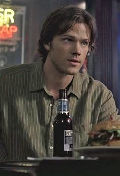 a man sitting at a table with a bottle of beer in front of him and a sandwich on the plate