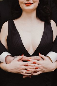 a woman with her arms crossed wearing a black dress and orange lipstick on her lips