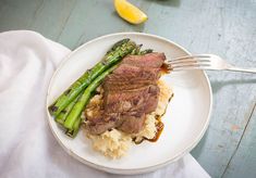 a white plate topped with meat and mashed potatoes covered in gravy next to asparagus