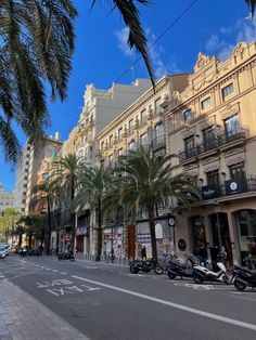 a city street lined with palm trees and parked motor scooters on the side