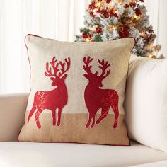 a white couch with a red reindeer pillow on it and a christmas tree in the background