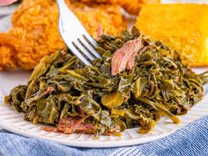 a white plate topped with collard greens next to fried cornbreads and ham