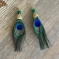 two pairs of peacock feathers with green beads and gold earwires on a wooden surface