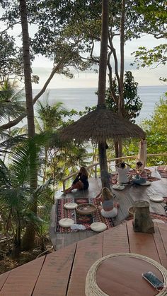 people are sitting on the deck in front of an umbrella and table with chairs around it