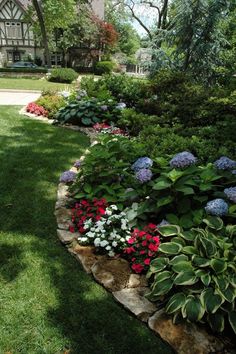 a garden filled with lots of flowers next to a lush green field and tree covered building