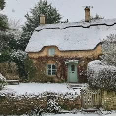 a house covered in snow next to a tree and shrubbery with a green door