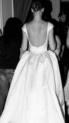 a woman in a white dress is walking down the aisle with other people behind her