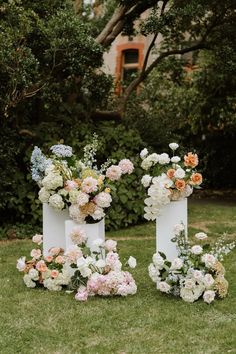 three white vases with flowers are sitting on the grass in front of some bushes