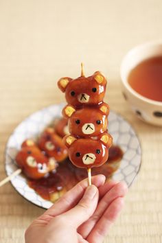 there is a hand holding some food on a stick with teddy bears on it and a cup of tea in the background