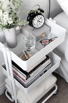 a white shelf with magazines and a clock on it next to a vase filled with flowers