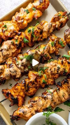 grilled chicken skewers on a tray with dipping sauces and parsley