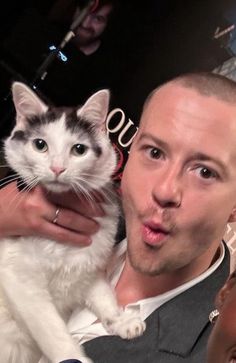 a man holding a white and black cat in his lap while making a funny face