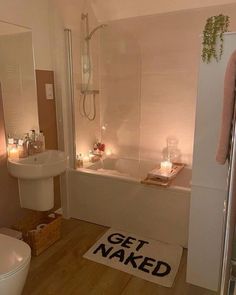 a bathroom with candles on the floor and a bathtub next to it, along with a rug that says get naked