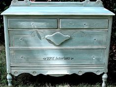 an antique dresser painted in pale blue and white with writing on the drawers, sitting in grass