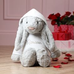 a stuffed rabbit sitting on top of a wooden floor next to a red rose bouquet