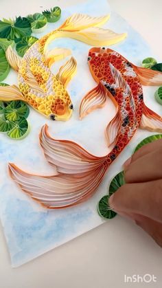 someone is painting two goldfishs on paper