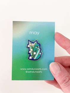 a person holding up a pin with flowers on it in their left hand and the words may above them