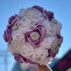 a bridal bouquet with purple and white flowers on it is being held by someone's hand