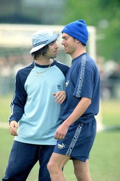 two young men standing next to each other on a soccer field, one wearing a blue hat