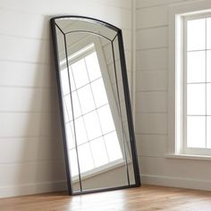 a large mirror sitting on top of a wooden floor next to a window in a room