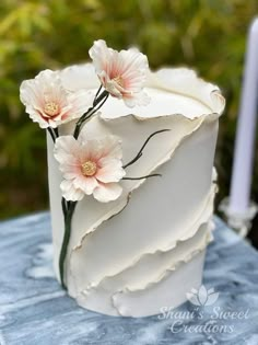 a white cake with pink flowers on it sitting on a blue tablecloth next to a lit candle