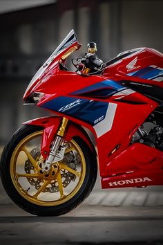 a red and blue motorcycle parked in front of a garage door with yellow rims