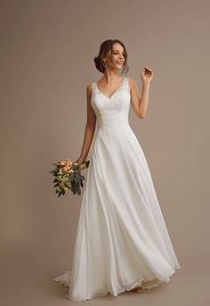 a woman in a white wedding dress holding a bouquet and posing for the camera with her hand up