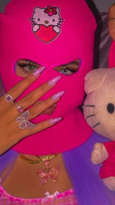 a woman wearing a pink hello kitty mask with her hands on her face next to a stuffed animal