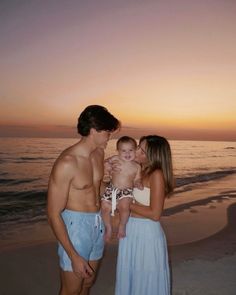 a man, woman and child standing on the beach at sunset