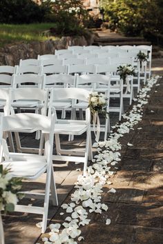 the aisle is lined with white chairs and petals on the ground for an outdoor ceremony