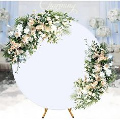 a round white sign with flowers and greenery on it, in front of a backdrop