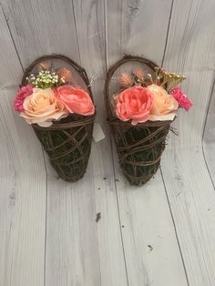 two baskets with flowers are sitting on a white wooden surface, one is made out of twigs and the other has pink roses