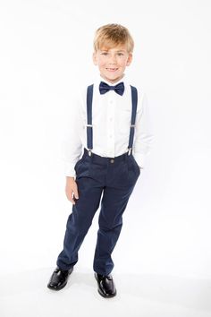 a young boy in a white shirt and blue pants is wearing a bow tie with suspenders