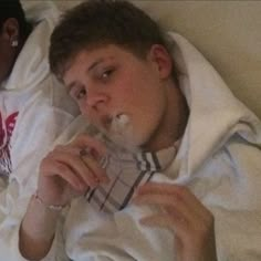 a man laying in bed with his mouth open and chewing something on his nose while wearing a hoodie